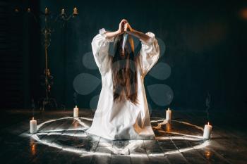 Woman with knife in hands sitting in pentagram circle with candles. Dark magic ritual, occultism and exorcism, supernatural power