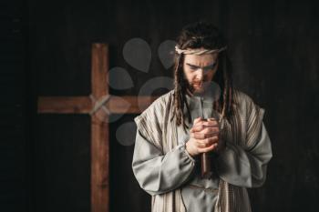 Man in the image of Jesus Christ praying with bible in hands, cross on black background. Prayer against crucifixion, christianity symbol
