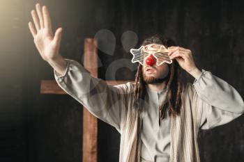 Man in the image of Jesus Christ in party glasses reaching out his hand, crucifixion cross on black background