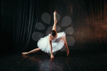 Grace of ballerina in white dress in motion on theatrical stage. Classical ballet dancer training in class with black background