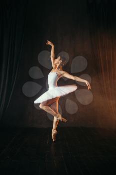 Elegance ballerina in white dress and pointe shoes dancing on theatrical stage. Classical ballet dancer training in class