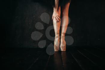 Female ballet dancer legs in pointes, black wooden floor. Ballerina in red dress and black practice dancing on the stage in theatre