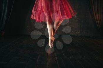 Female ballet dancer legs in pointes. Ballerina in red dress and black practice dancing on the stage in theatre