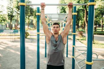 Male athlete doing exercise on horizontal bar on outdoor fitness workout. Strong sportsman on sport training in park