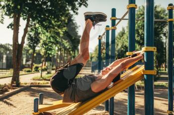 Man in sportswear doing exercise on press using horizontal bar, outdoor fitness workout. Strong sportsman on sport training in park