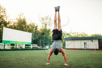 Male athlete standing on hands upside down, outdoor fitness workout. Strong sportsman in park