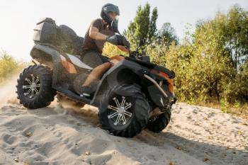 Atv freeriding in sand quarry, extreme sport. Male driver in helmet riding on quad bike in sandpit