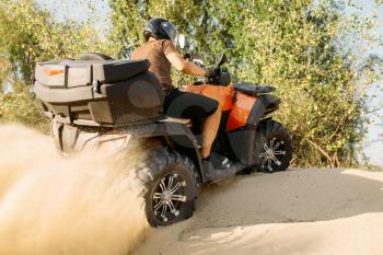 Atv riding in action, sand quarry on background, extreme sport. Male driver in helmet on quad bike in sandpit