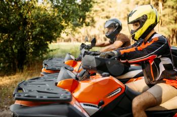 Two atv riders in helmets before the trip, side view, summer forest on background. Male quadbike drivers, atv riding, active travelling
