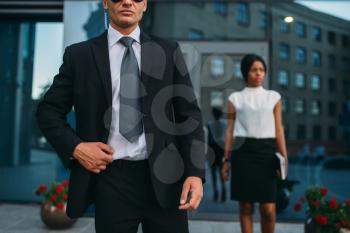 Bodyguard in suit and sunglasses, female VIP client on background. Security guard is a risky profession, professional guarding, business persons protection