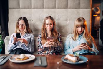 Three girls sitting on the couch and using mobile phones in cafe. Chocolate dessert and alcohol on the table
