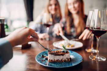 Young women eats sweet cakes in restaurant. Chocolate dessert and alcohol on the table