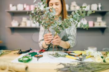 Female florist prepares flower composition, garden equipment on workplace. Flower shop, floral business