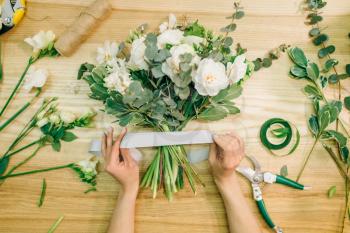 Female florist hands cuts flower composition with pruner, top view. Floral business, decoration tools