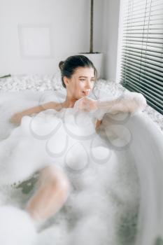 Sexy woman lying in bath with foam, relaxation in luxury bathroom with stone decor