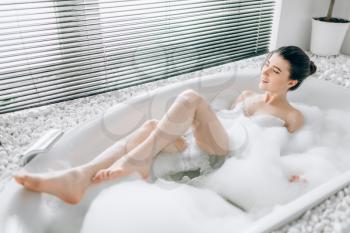 Young woman lying in bath with foam, blured view relaxation in luxury bathroom with stone decor
