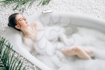 Attractive lady lying in bath with foam, top view. Relaxation, health and skin care in bathroom, spa