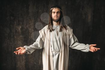 Jesus Christ in white robe praying with open arms, dark background. Son of God, christian faith