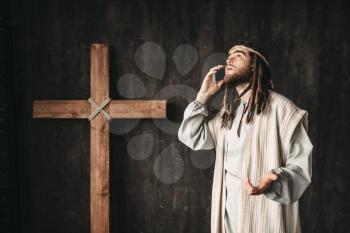 Man in the image of Jesus Christ talking to God by mobile phone, crucifixion cross on black background