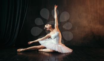 Grace of ballerina in white dress in motion on theatrical stage. Classical ballet dancer training in class with black background