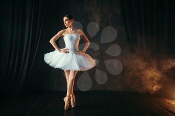 Elegance ballerina in white dress and pointe shoes dancing on theatrical stage. Classical ballet dancer training in class