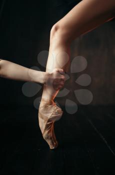 Ballerina hand holds the foot in pointe shoes, black wooden floor. Ballerina in red dress and black practice dancing on the stage in theatre