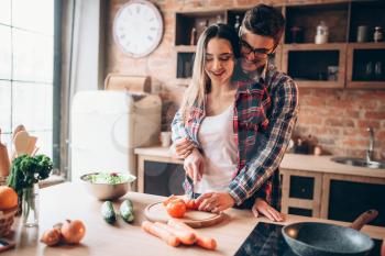 Couple hugs while cooking fresh vegetable salad in bowl on the kitchen. Diet food preparation. Couple prepares romantic dinner, healthy lifestyle