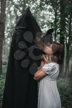 Death in a black hoodie takes the soul of young female victim, forest on background. Photo in horror style, mystery ritual