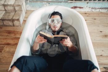 Funny businessman in flippers and mask lies in bathtub and reads a book, humor. Business lottery concept