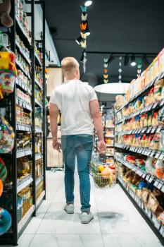 Male customer with basket choosing food in supermarket. Shopping in food store