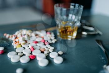Junkie kit, narcotic concept, addiction problem. Pills are laid out on wooden table, alcohol and handcuff
