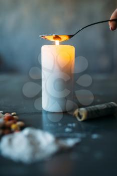 Druggy warms the dose in a spoon on fire from the candle, addiction problem concept. Pills are laid out on wooden table, narcotics