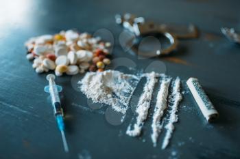 Junky kit, narcotics concept, addiction problem. Pills are laid out on wooden table, syringe for dose, alcohol and handcuff, top view