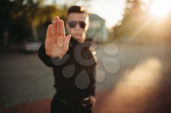 Serious police officer in uniform and sunglasses shows a hand stop sign, front view. Cop at the work. Law protection concept, safety control job