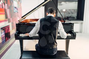 Male pianist playing composition on grand piano, back view. Musician practicing melody at the royale, classical musical instrument