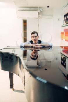 Male pianist at the classical black grand piano with perfectly polished surface. Performer poses at the royale keyboard, musical instrument