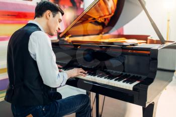 Male pianist at the classical black grand piano, performance in studio. Musician plays melody at the royale keyboard, musical instrument