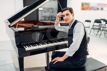 Professional pianist at the classical black grand piano, performance in studio. Performer poses at the royale keyboard, musical instrument