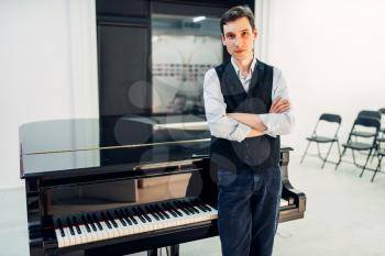 Male pianist stands at the black grand piano, front view. Musician poses at the classical royale, keyboard musical instrument
