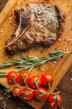 Juicy grilled steak on the bone and tomatoes on a branch closeup, nobody. Meat dish on wooden table