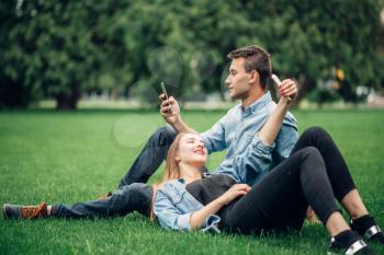 Phone addicted people, couple lies on the grass and using their smartphones, social addict