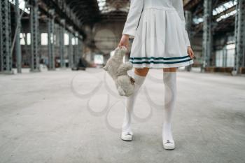 Cute anime style blonde woman with toy bear in hand. Cosplay, japanese culture, doll in dress on abandoned factory