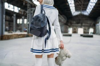 Anime style blonde woman looks at the toy bear. Cosplay girl, japanese culture, doll in dress on abandoned factory