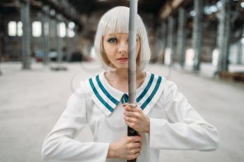 Pretty anime style blonde girl with sword. Cosplay fashion, asian culture, doll with blade on abandoned factory, cute woman with makeup