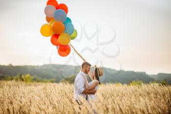 Love couple with colorful air balloons in a rye field. Pretty woman on summer meadow