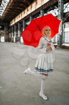 Pretty anime style blonde girl with red umbrella. Cosplay fashion, asian culture, doll in dress, cute woman with makeup in the factory shop
