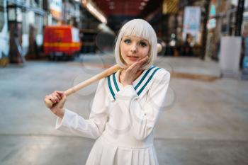 Cute anime style blonde girl with baseball bat. Cosplay fashion, asian culture, doll in dress, sexy woman with makeup in the factory shop