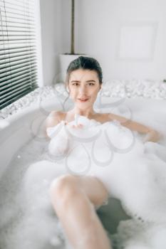 Sexy woman lying in bath with foam, relaxation in luxury bathroom with stone decor