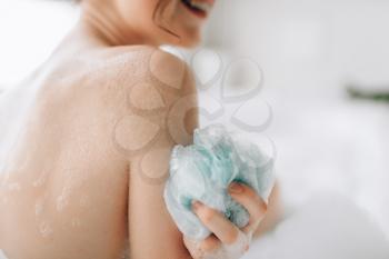 Female person soaps the body with a sponge in bath. Bodycare and skincare in bathroom