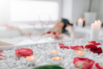 Woman lying in the bath with foam, rose petals, burning candles. Full relaxation, romantic setting in bathroom